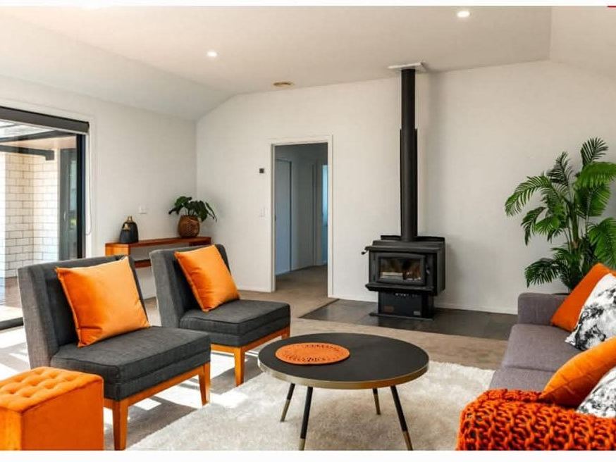 Staged lounge with grey armchairs and orange cushions beside a log burner