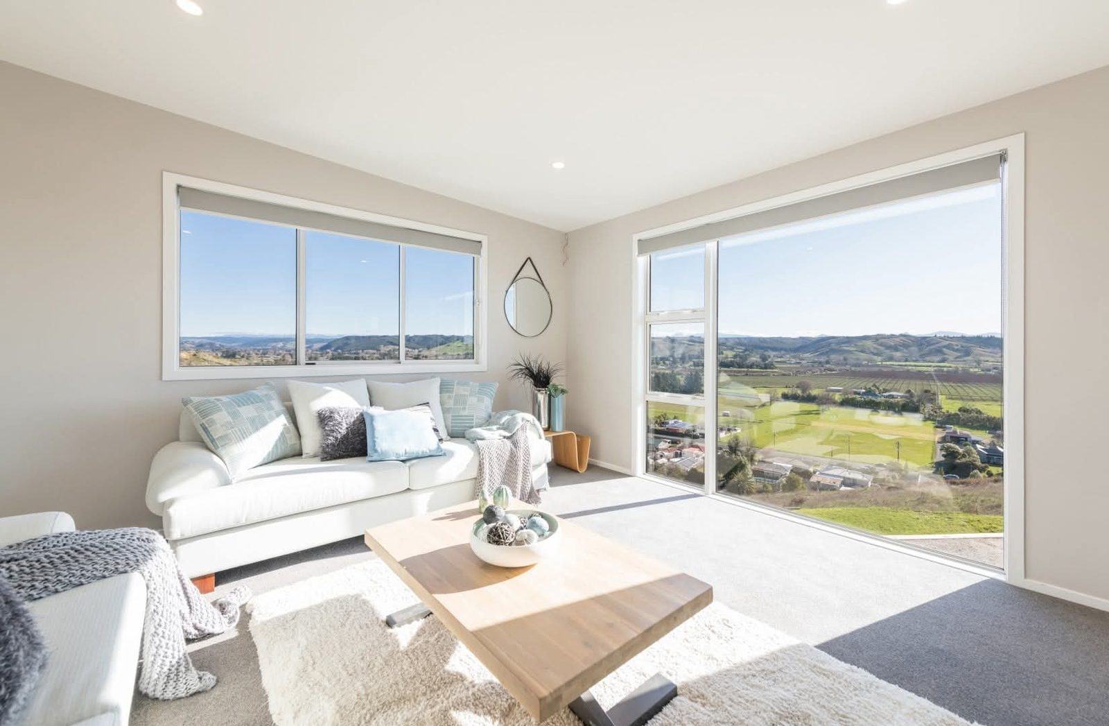 A staged living room with white sofa and sweeping views over the Tasman countryside